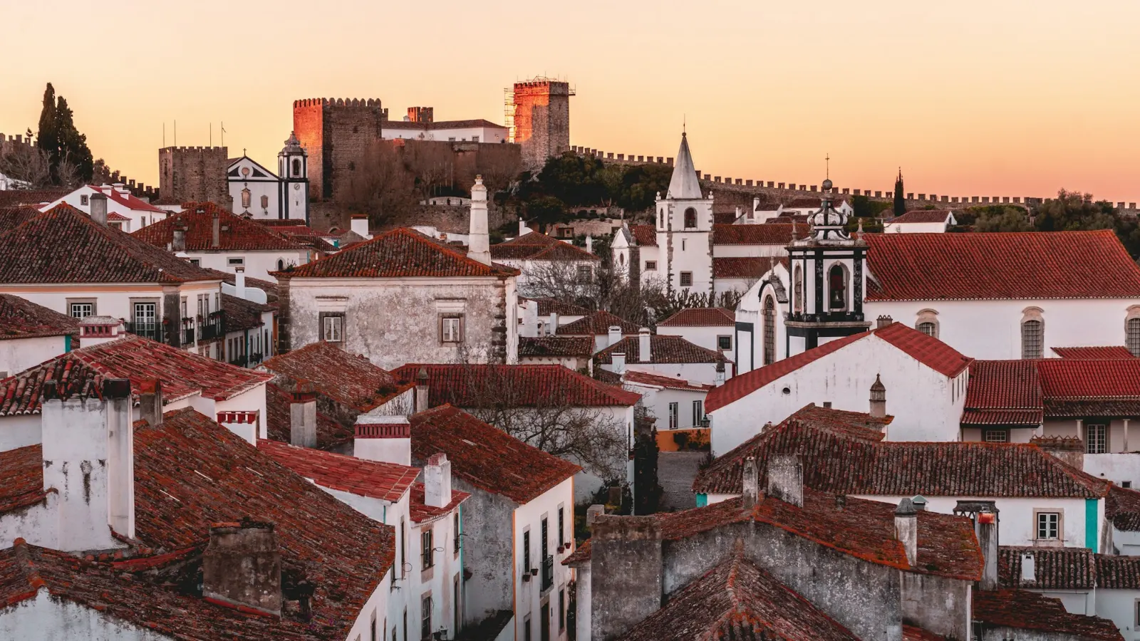Casario branco com telhados de telha e muralhas de Óbidos ao pôr do sol, aldeia típica portuguesa